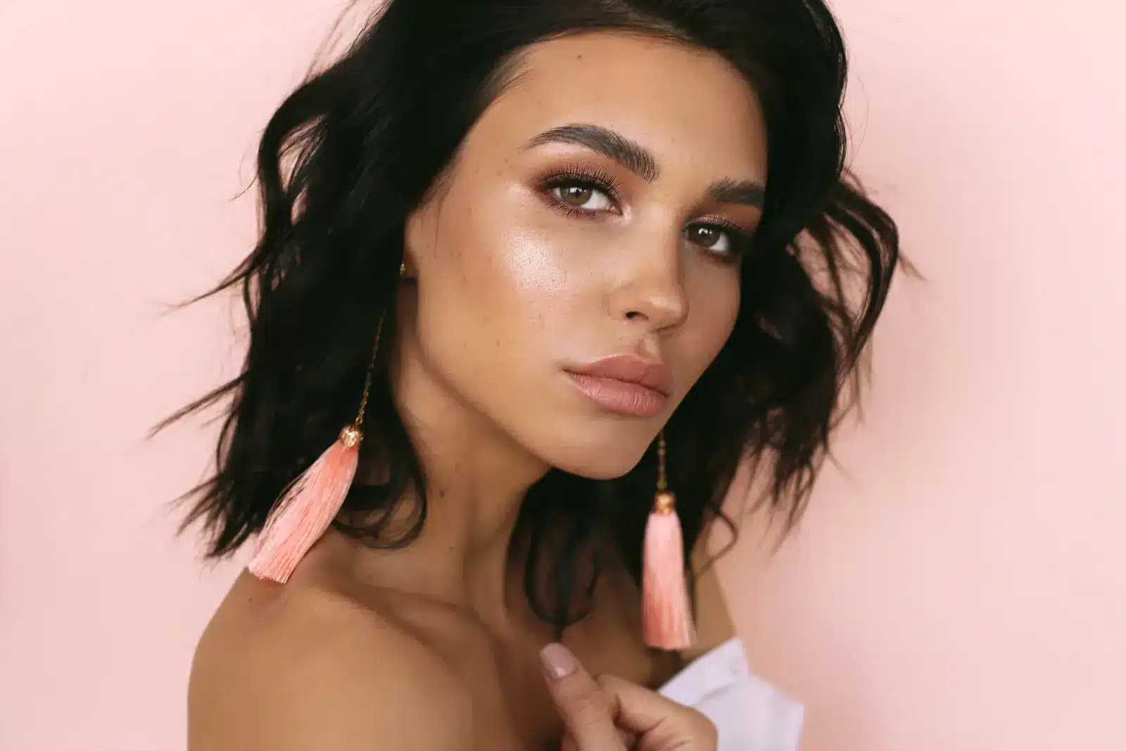 Woman with glowing skin and tassel earrings against pink background